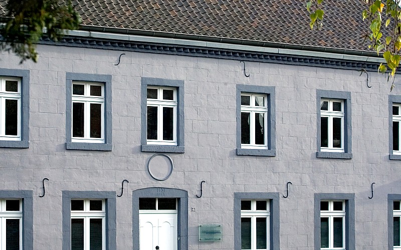Fassade eines historischen Wohnhauses mit weißen Sprossenfenstern und grauer Putzoptik