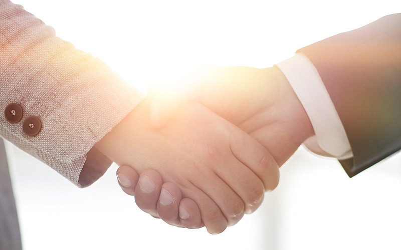 Zwei Menschen geben sich die Hand bei hellem Gegenlicht – symbolisch für Vertrauen, Einigung oder Partnerschaft